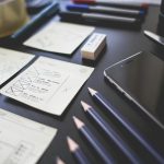 A creative workspace featuring UI design plans, pencils, a smartphone, and other office tools.