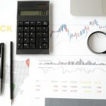 Flat lay of stock market analysis tools including calculator, graphs, and magnifying glass.