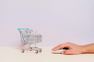 Conceptual image of a hand on a mouse next to a miniature shopping cart filled with ice cubes, symbolizing online shopping.