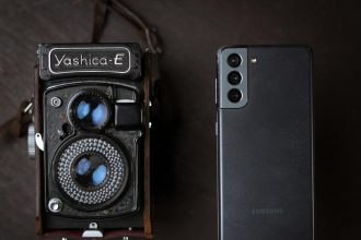 A vintage Yashica camera next to a modern smartphone, showcasing old and new technology.