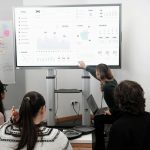 Group of professionals engaged in a business presentation examining charts on a large screen.