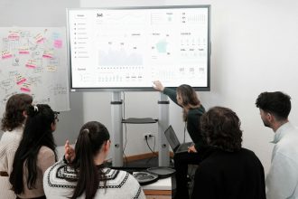 Group of professionals engaged in a business presentation examining charts on a large screen.
